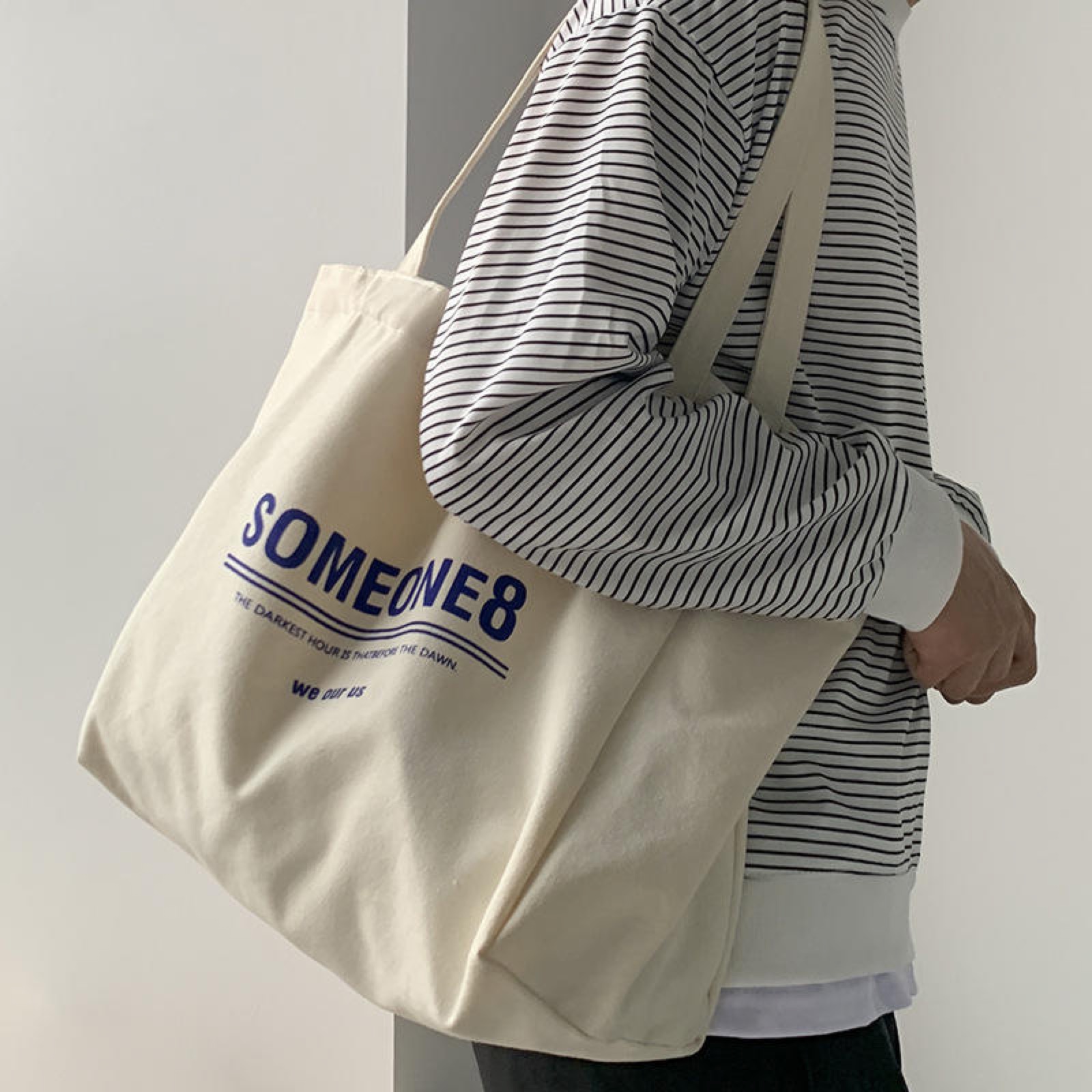 Model carrying a large natural canvas tote bag over the shoulder